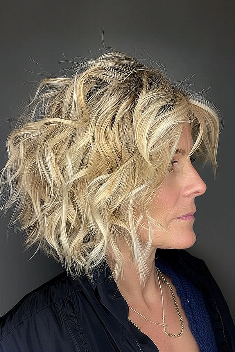 Side view of a woman with a blonde angled bob featuring soft waves and balayage highlights