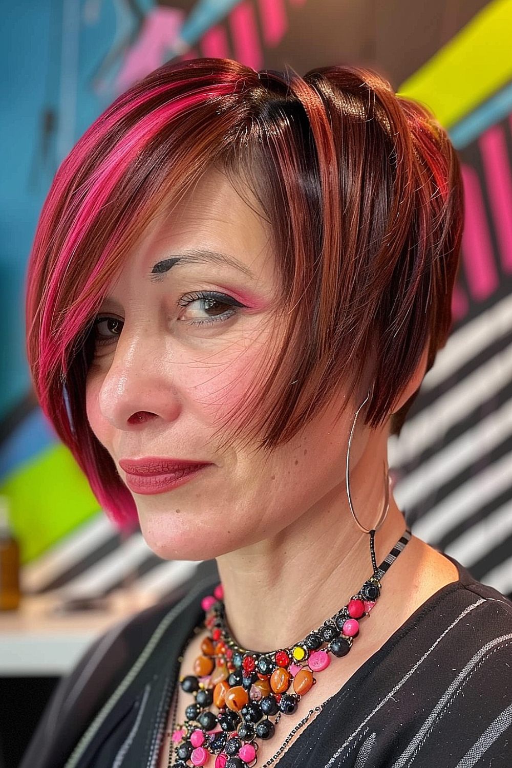 Woman with an asymmetrical bixie haircut featuring bold streaks of pink and red on a brunette base