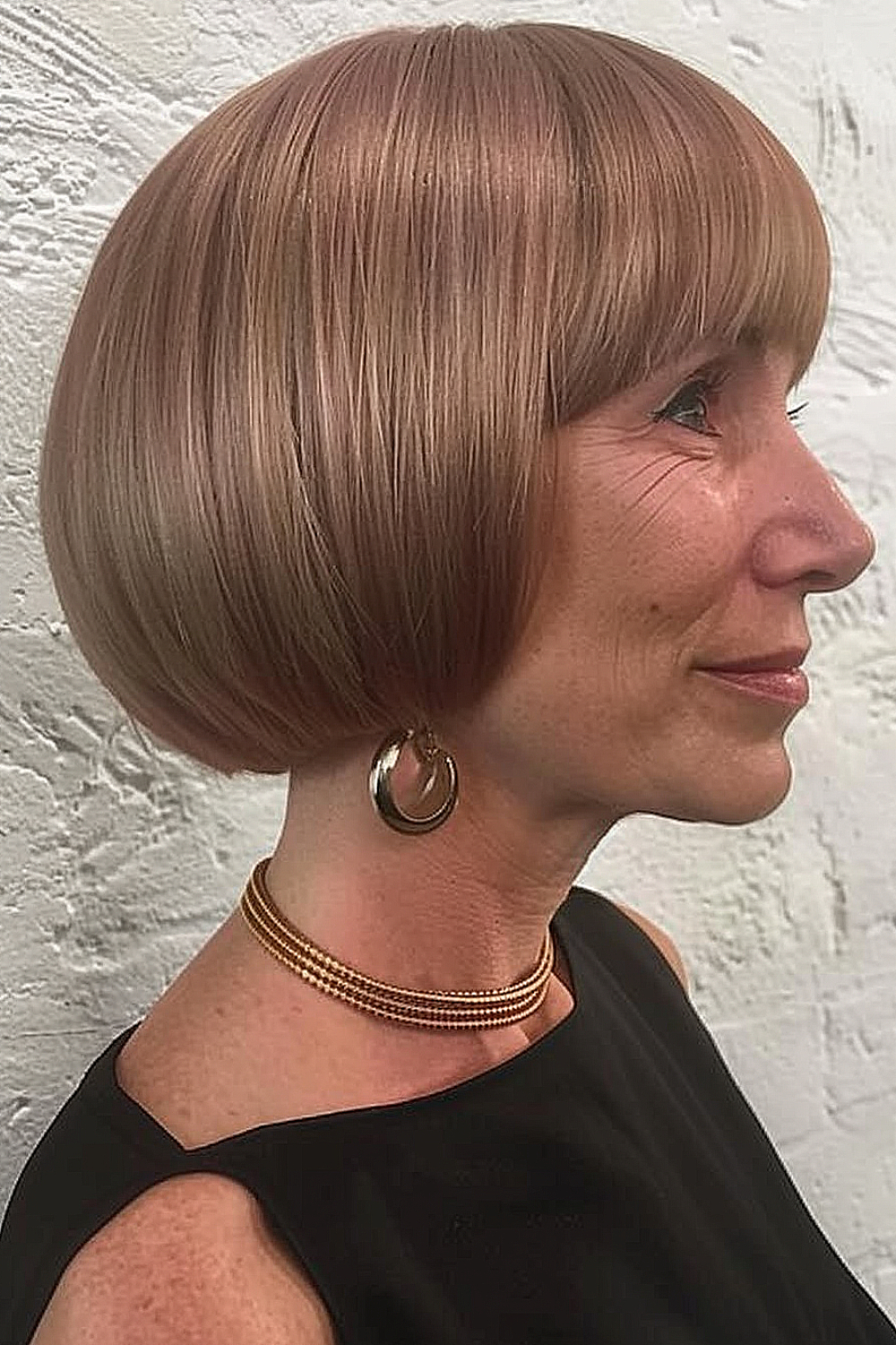 A woman with a classic pageboy haircut in a strawberry blonde hue, radiating timeless elegance