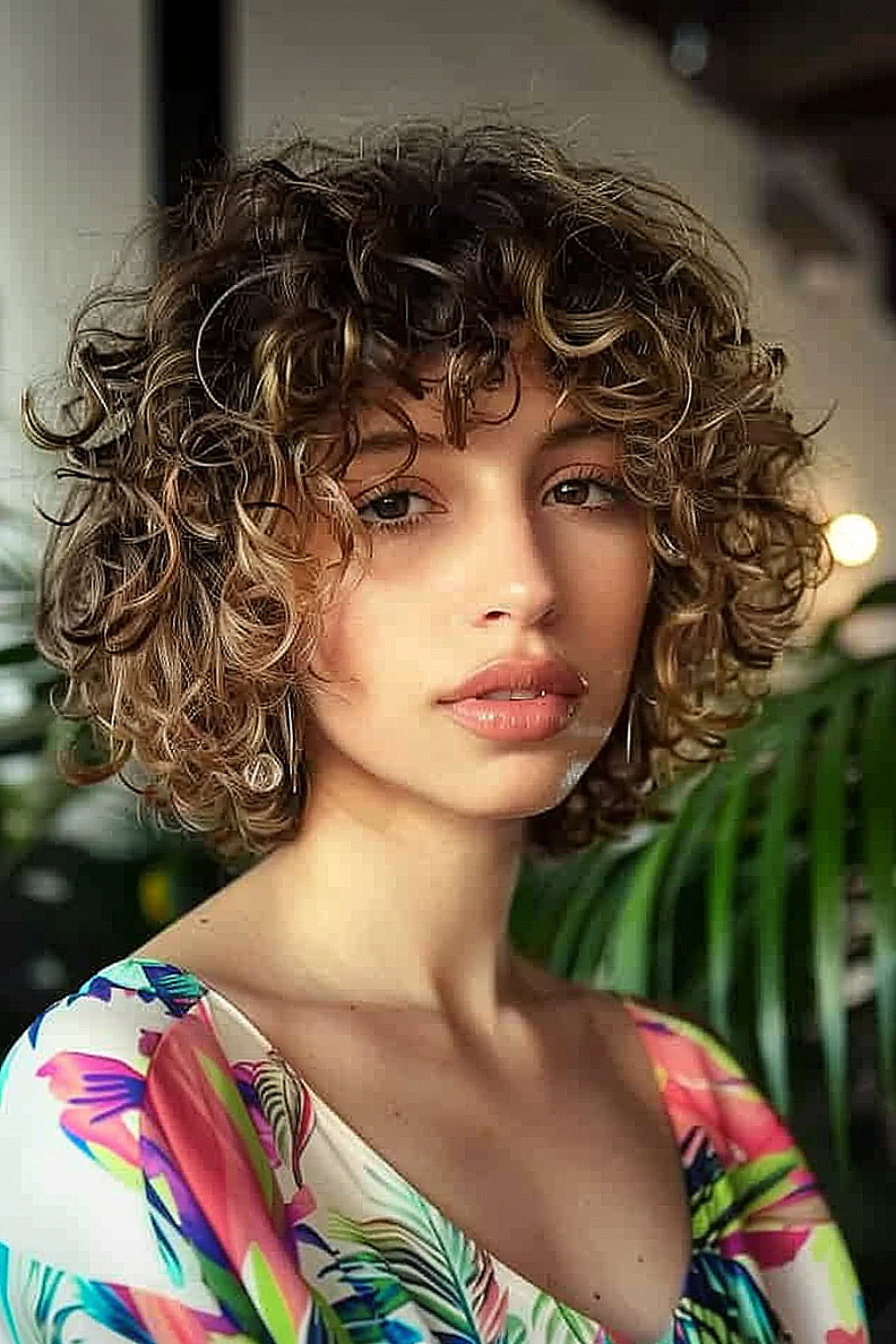 Woman with a curly bob and bangs, featuring caramel highlights