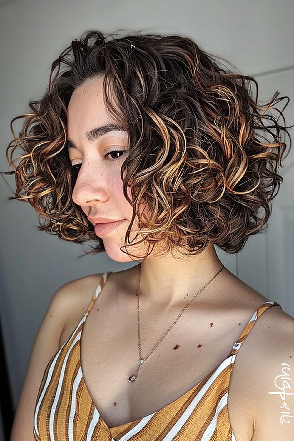 Woman with a curly bob hairstyle featuring caramel highlights