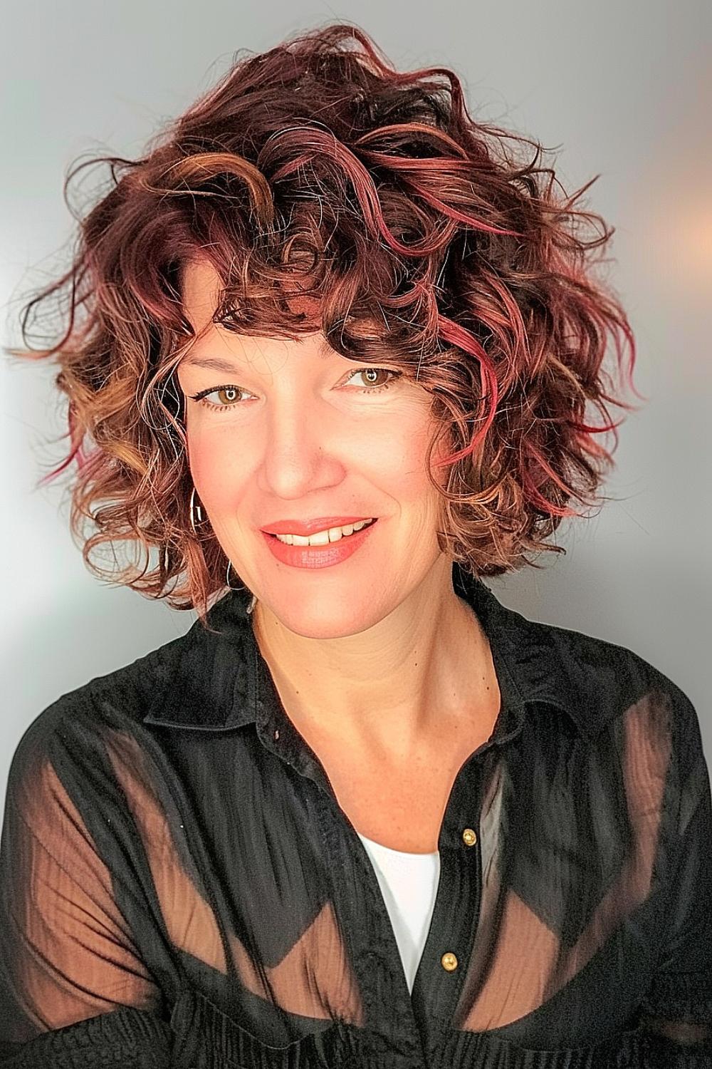 Woman with a curly bob and side-swept bangs in shades of burgundy and red