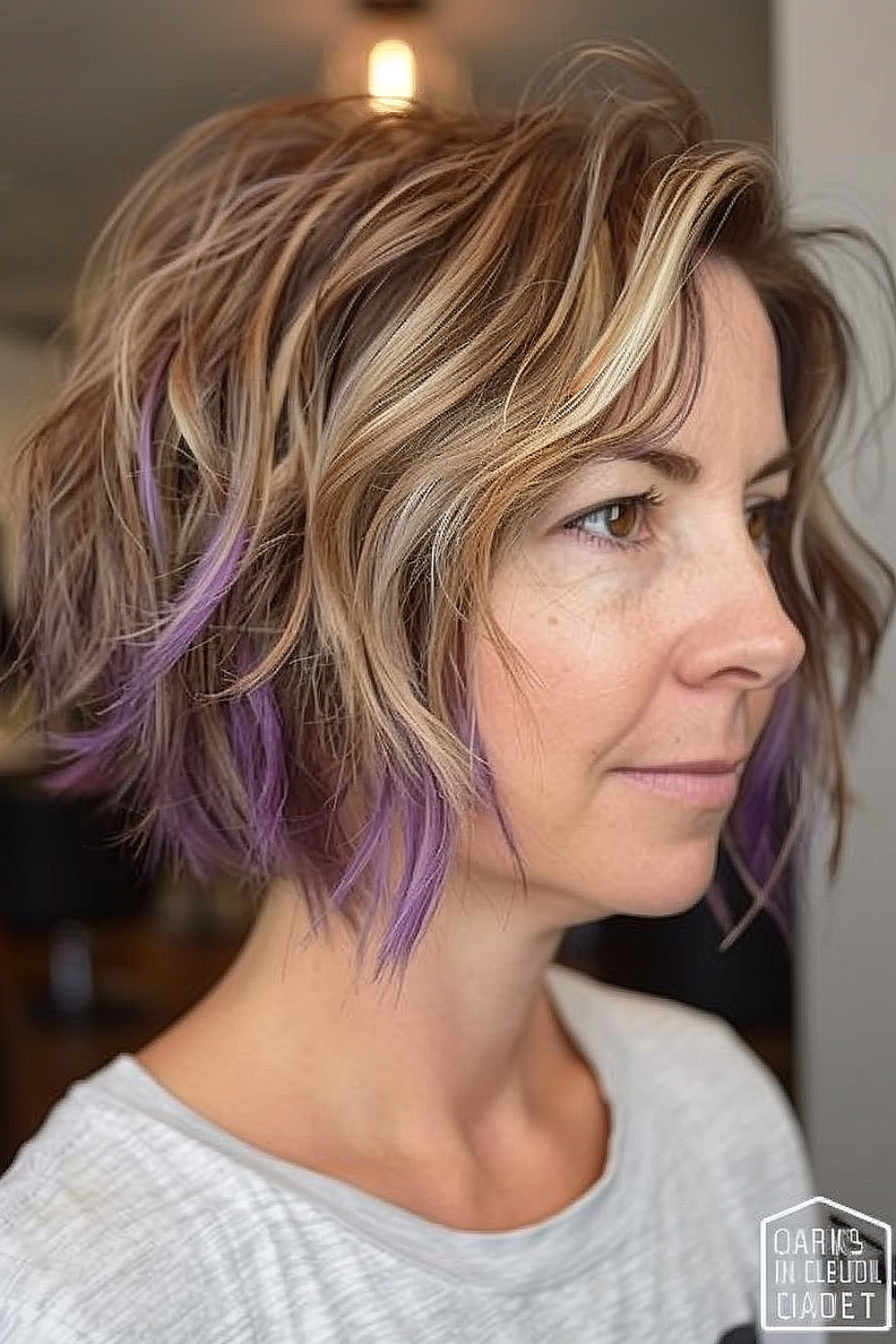 Woman with a shaggy bob featuring peek-a-boo purple highlights among blonde and brown hair