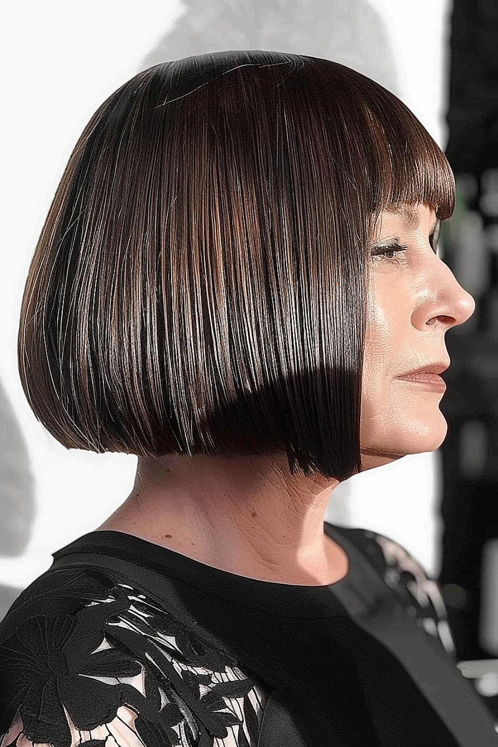 Woman with a sleek short blunt bob and straight-across edgy bangs in a deep brunette shade