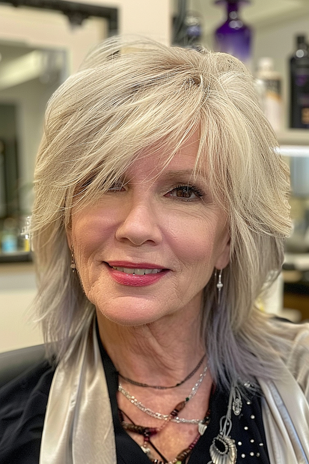 A woman over 60 with a soft shag haircut featuring side-swept fringe and multi-tonal blonde shades