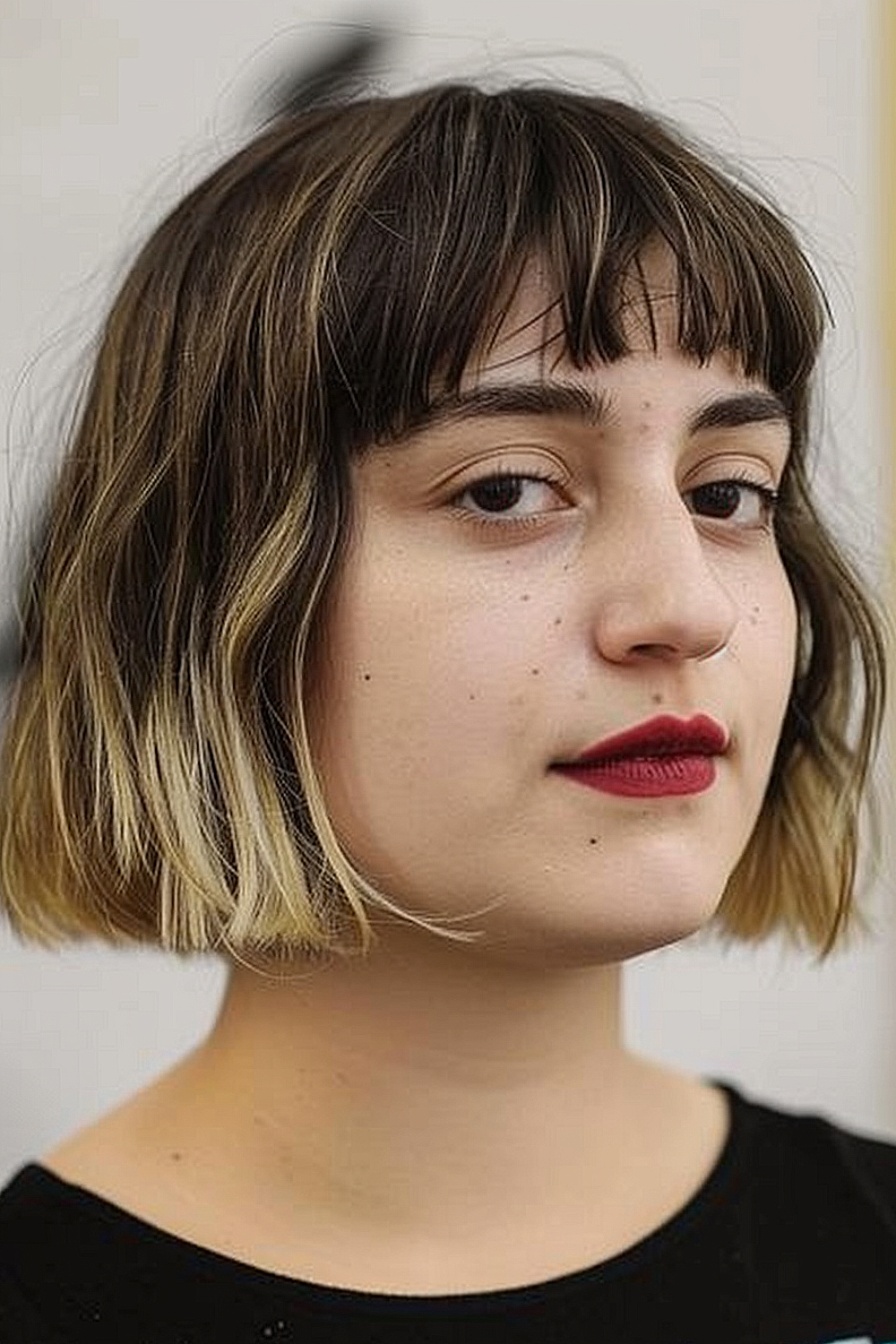 Woman with a textured bob featuring choppy layers and micro bangs, transitioning from brunette to blonde