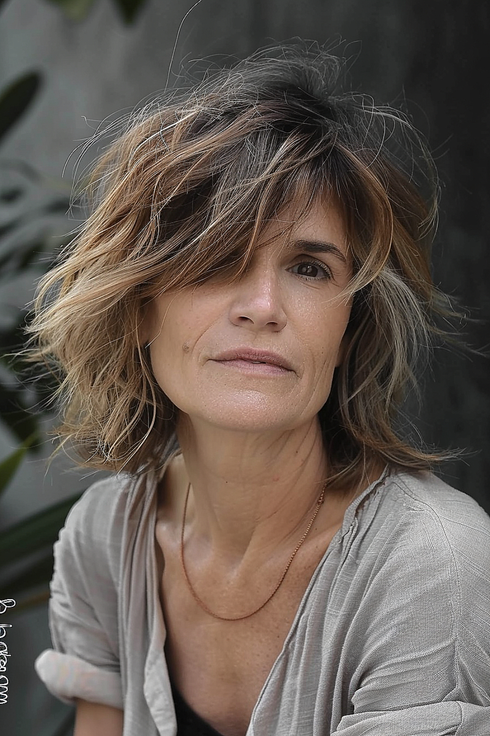 Woman with a tousled shag haircut and side-swept bangs in mixed brunette and blonde tones